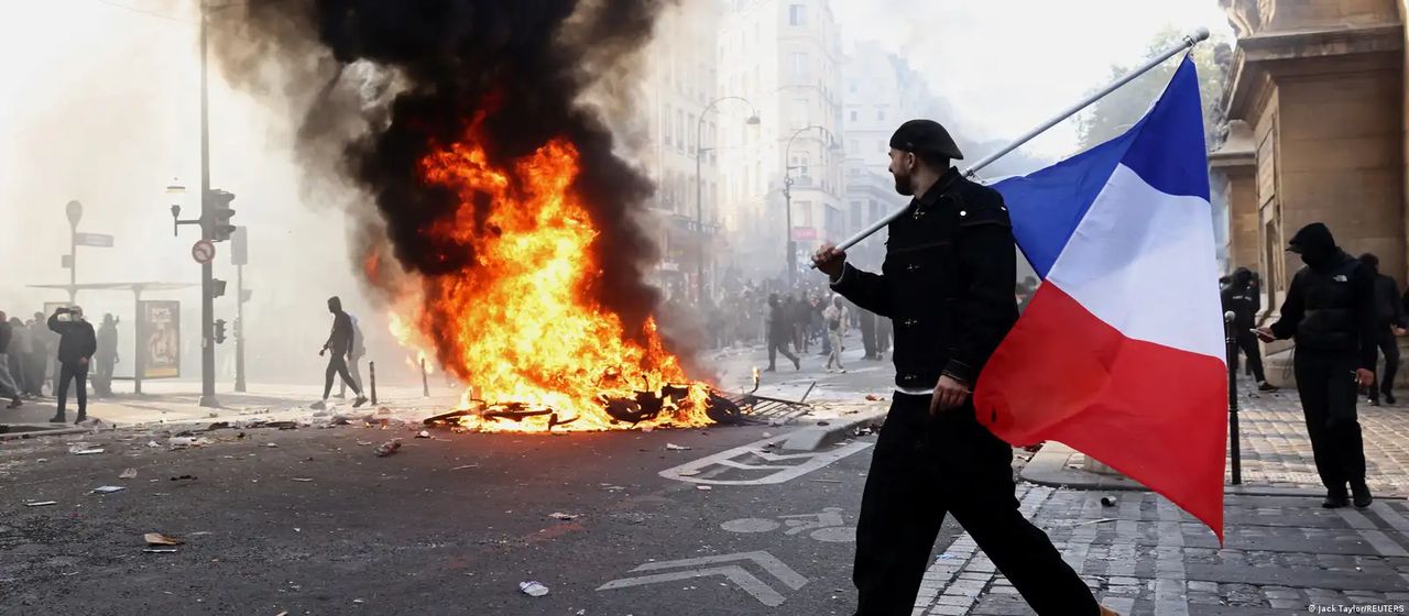 Un hombre camina con una bandera francesa junto a una barricada en llamas en una calle de París